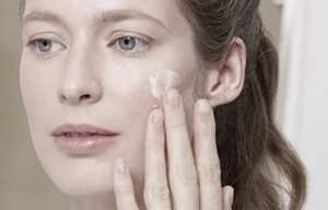 Mujer aplicándose crema en la mejilla derecha.