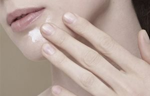 Mujer aplicándose crema en la barbilla.